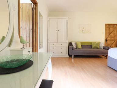 A room with a glass table, a white wardrobe, a gray sofa with green pillows, and a wooden door at Ty Newydd in Llangadfan