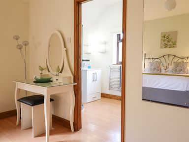 A dressing table with a mirror and stool next to an open door showing a bathroom and a reflection of a bedroom at Ty Newydd in Llangadfan