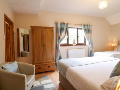 A bedroom with two beds a wooden wardrobe a beige chair and a window with curtains at Ty Newydd in Llangadfan