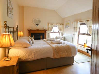 A bedroom with a double bed bedside table lamps fireplace armchair and two windows at Ty Newydd in Llangadfan