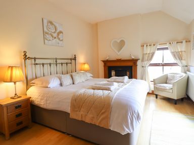 A bedroom with a double bed two bedside lamps an armchair and a fireplace at Ty Newydd in Llangadfan