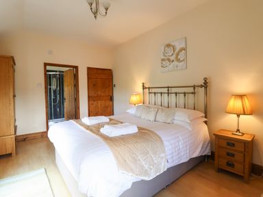 A bedroom with a double bed pillows bedside tables lamps wooden doors and wardrobe at Ty Newydd in Llangadfan