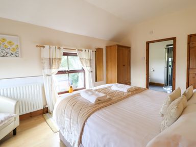 A bedroom with a bed with pillows and towels a window with curtains a wooden wardrobe and an en suite bathroom at Ty Newydd in Llangadfan