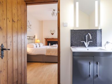 A bedroom with a bed and a fireplace visible through an open wooden door next to a bathroom sink with a mirror and lights at Ty Newydd in Llangadfan