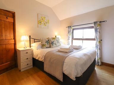 A bedroom with a double bed with floral pillows bedside tables with lamps and a window with floral curtains at Ty Newydd in Llangadfan