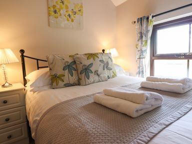 A bedroom with a bed with floral pillows and folded towels bedside lamps and window with floral curtains at Ty Newydd in Llangadfan