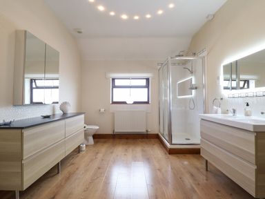 A bathroom with wooden floor cabinets a shower area a toilet and a window at Ty Newydd in Llangadfan