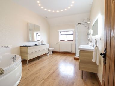 A bathroom with a bathtub a wooden vanity with mirrors a toilet a shower and a sink with a mirror at Ty Newydd in Llangadfan