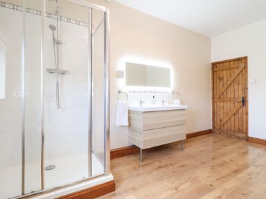 A bathroom with a glass shower enclosure a wooden door and a double sink vanity with a backlit mirror at Ty Newydd in Llangadfan