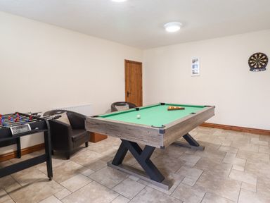 A game room with a pool table foosball table two chairs and a dartboard on the wall at Ty Newydd in Llangadfan