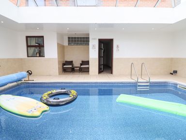 An indoor swimming pool with inflatables two chairs and a table on the tiled poolside at Ty Newydd in Llangadfan