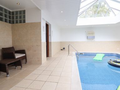 An indoor pool with a skylight above and two chairs against the tiled wall at Ty Newydd in Llangadfan