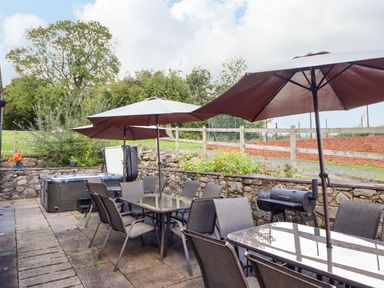 An outdoor patio with glass tables chairs umbrellas a barbecue and a hot tub at Ty Newydd in Llangadfan