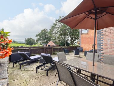 An outdoor patio with lounge chairs dining table chairs umbrella and a wooden fence at Ty Newydd in Llangadfan