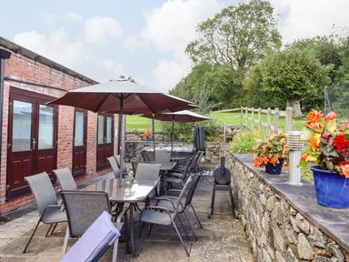 An outdoor patio with dining tables and umbrellas next to a brick building and flower pots on a stone wall at Ty Newydd in Llangadfan