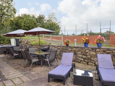 An outdoor patio with chairs tables umbrellas and flower pots on a stone wall at Ty Newydd in Llangadfan