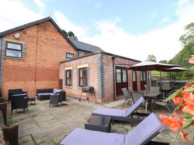 An outdoor patio area with lounge chairs, tables, umbrellas, and a barbecue grill at Ty Newydd in Llangadfan