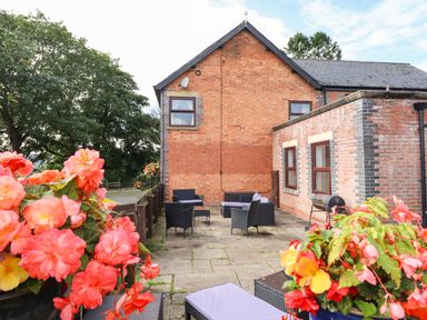 An outdoor patio area with wicker chairs and tables a barbecue grill and potted flowers next to a brick house at Ty Newydd in Llangadfan