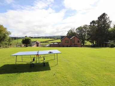 A ping pong table on a lawn with a brick house and trees in the background at Ty Newydd in Llangadfan