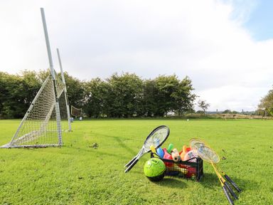 A grassy sports field with two soccer goals and a crate of sports equipment including rackets and balls at Ty Newydd in Llangadfan