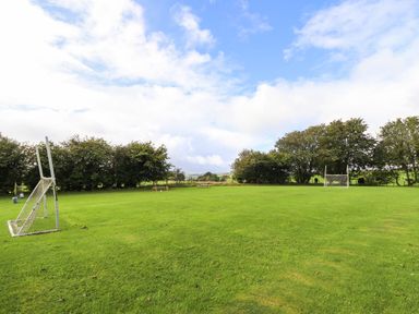 A grassy sports field with two goalposts and trees in the background at Ty Newydd in Llangadfan
