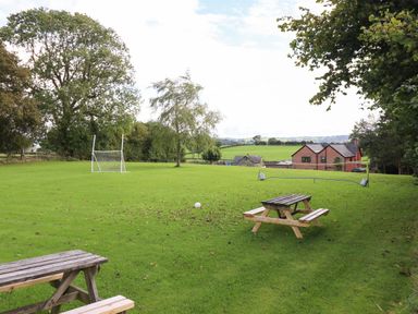 A grassy field with picnic benches a soccer goal and a badminton net near a red brick house at Ty Newydd in Llangadfan