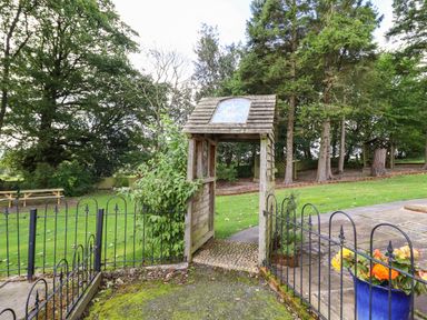 A garden area with a wooden archway gate black metal fence flowers in a blue pot and trees at Ty Newydd in Llangadfan