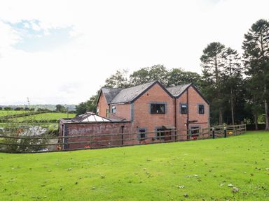 A brick house with a fenced green lawn and trees at Ty Newydd in Llangadfan