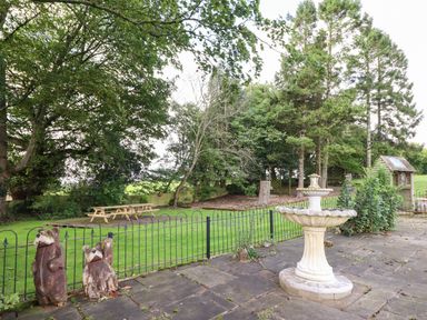 A garden with a stone fountain a paved area wooden bear sculptures and a picnic table at Ty Newydd in Llangadfan