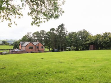 A large green lawn with a brick house and trees in the background at Ty Newydd in Llangadfan