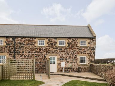 Exterior view of a stone house with six windows a door and a small fenced paved area at High Hemmel House in Embleton