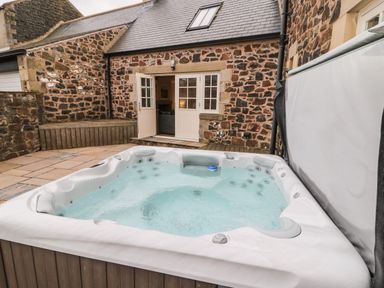 An outdoor hot tub in a stone walled patio area with an open door leading into a building at High Hemmel House in Embleton