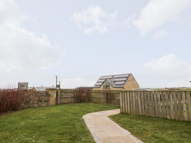 A garden with a stone path and wooden fences with a house in the background at High Hemmel House in Embleton