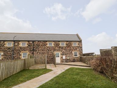 The exterior of a stone building with multiple windows a door a paved pathway and grassy areas at High Hemmel House in Embleton