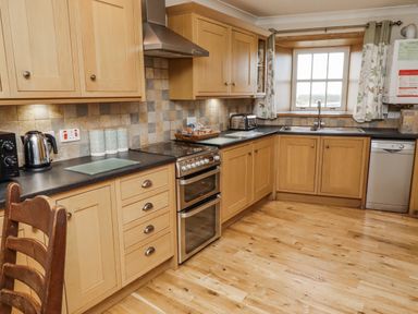 A kitchen with wooden cabinets, appliances, and countertop at High Hemmel House in Embleton