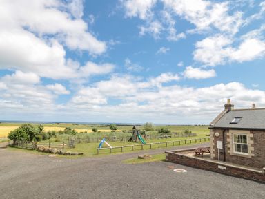 A playground with slides and benches near a brick building in an open field at Home Stead Cottage in Embleton