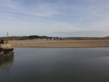 A body of water with a concrete structure labeled slow speed and a sandy shore with houses and hills in the distance at Tiggy Winkle St Merryn near Padstow