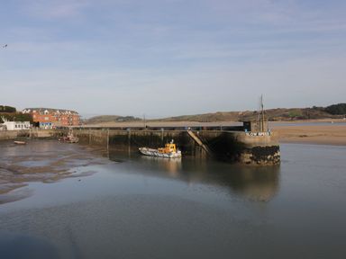 A harbor with boats docked near a concrete pier and buildings in the background at Tiggy Winkle in St Merryn near Padstow