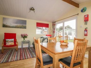 A dining area with a wooden table and chairs and a sitting area with a red armchair and a green sofa at Tiggy Winkle in St Merryn near Padstow