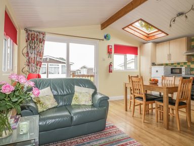 A living area with a green leather sofa and a wooden dining table with chairs near a kitchen at Tiggy Winkle in St Merryn near Padstow