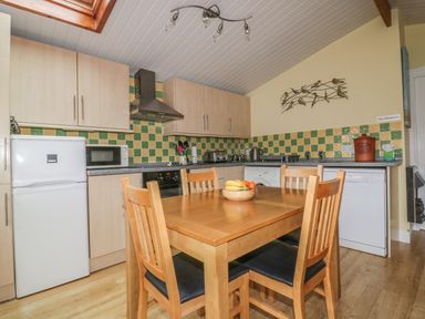 A kitchen with wooden dining table and chairs appliances and tiled backsplash at Tiggy Winkle in St Merryn near Padstow