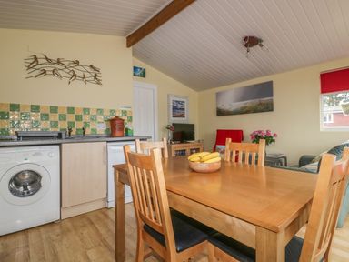A kitchen and dining area with wooden table and chairs bananas on table washing machine and colorful tiled backsplash at Tiggy Winkle in St Merryn near Padstow