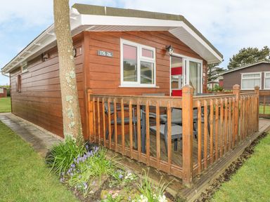 Exterior of a wooden cabin with a small fenced porch and garden at Tiggy Winkle in St Merryn near Padstow