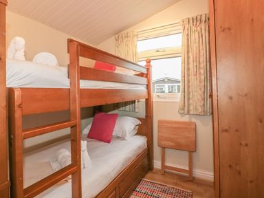 A bedroom with wooden bunk beds a small wooden folding table and a wardrobe at Tiggy Winkle in St Merryn near Padstow