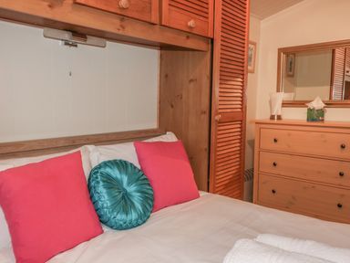 A bedroom with a bed with pillows and a wooden dresser with a mirror at Tiggy Winkle in St Merryn near Padstow