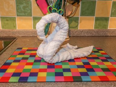 A kitchen countertop with a towel folded into a swan shape on a multicolored mat and kitchen utensils in a container in the background at Tiggy Winkle in St Merryn near Padstow