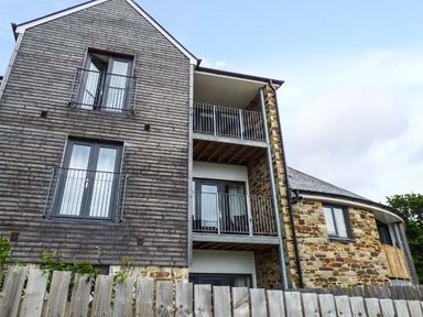 A multi-story building with wood and stone exterior walls and balconies behind a wooden fence at Tehidy in Charlestown