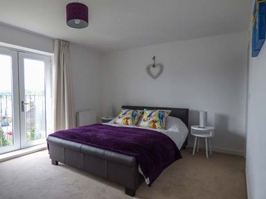 A bedroom with a double bed covered with a purple blanket and decorative pillows next to two round white bedside tables at Tehidy in Charlestown