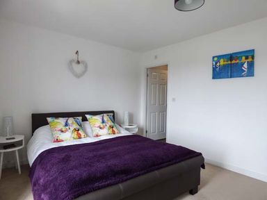 A bedroom with a bed with colorful pillows and purple blanket white walls and side tables at Tehidy in Charlestown