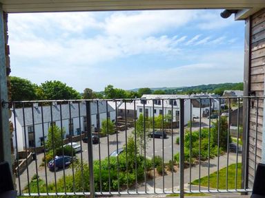 A balcony with metal railing overlooking a residential area with white houses and parked cars at Tehidy in Charlestown